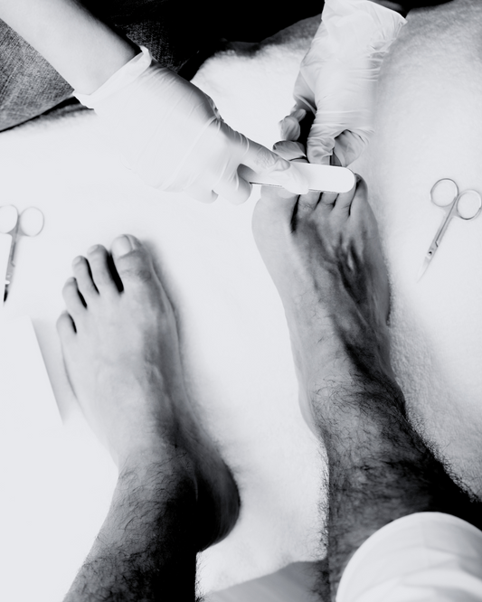 BLACK AND WHITE IMAGE OF A MANS FEET. HE IS GETTING A PEDICURE