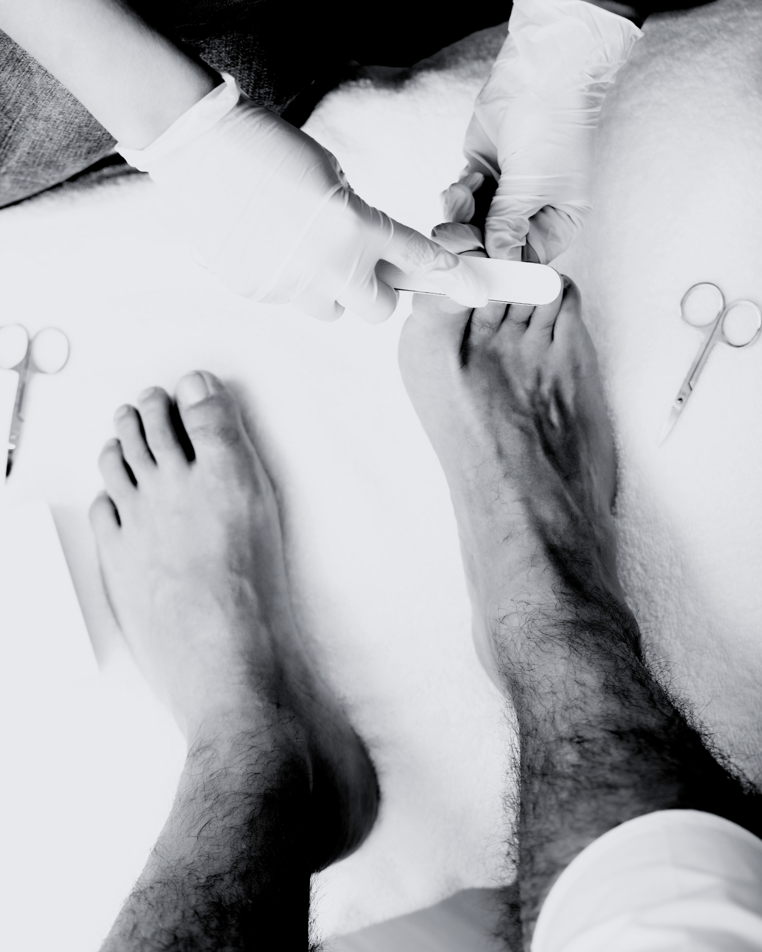 Black and white image of a medical procedure being performed on a mans feet and legs.