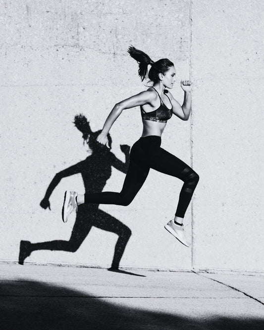 Black and white image of a woman running.  Her shadow is prominent on the wall behind her