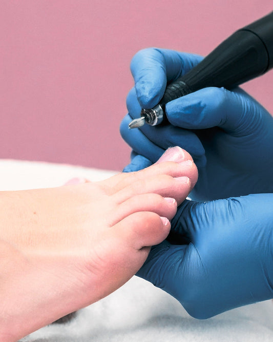 A nail technicians hands performing a medical pedicure on a foot